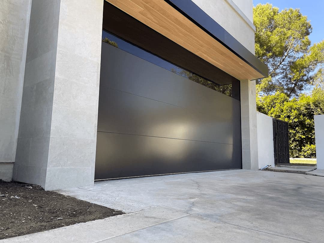 Flush graphite modern garage door with a wood-clad overhang on a stone-faced home