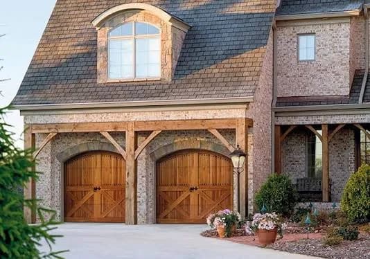 Amarr Classica wood-look carriage-house garage doors with X-brace detailing under timber arches on a brick home