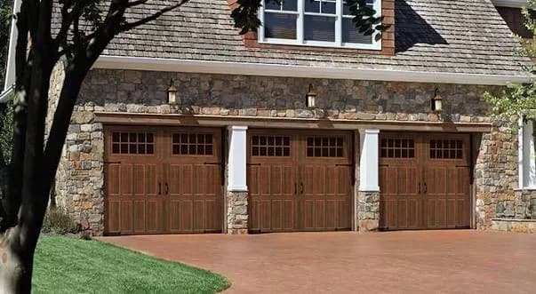 Three brown stamped carriage-house garage doors with arched divided-light windows on a stone home