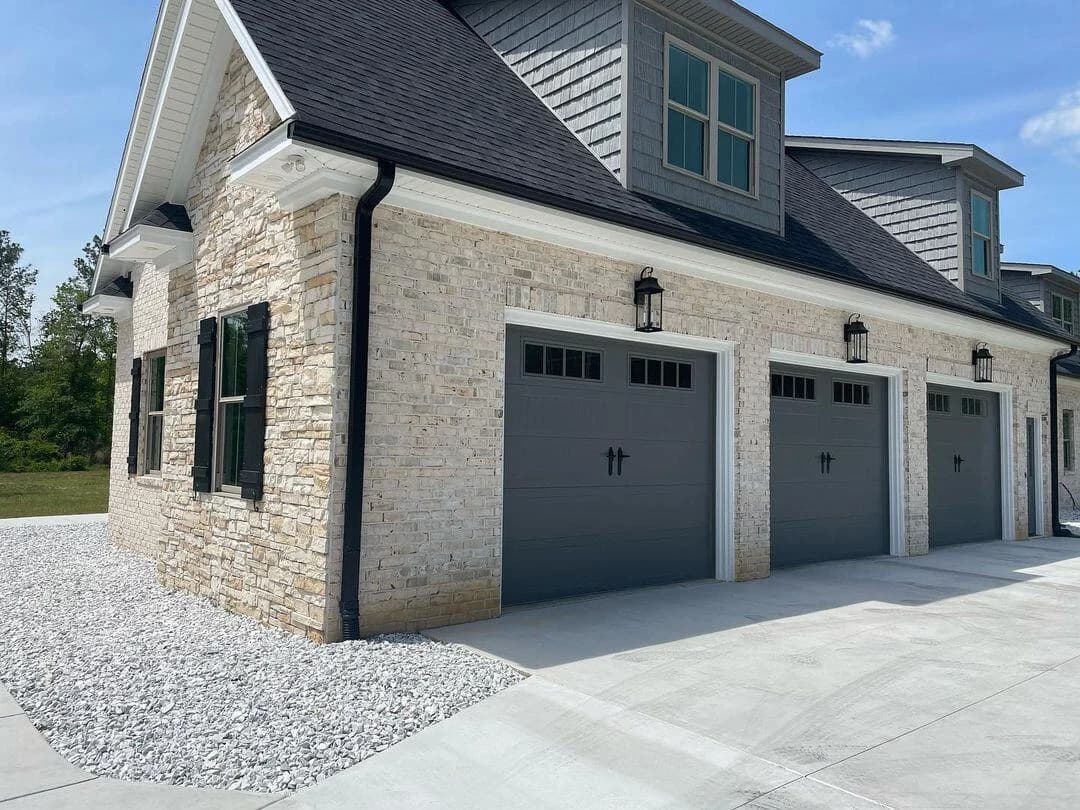 Charcoal recessed-panel garage doors on a light stone home with black coach lanterns