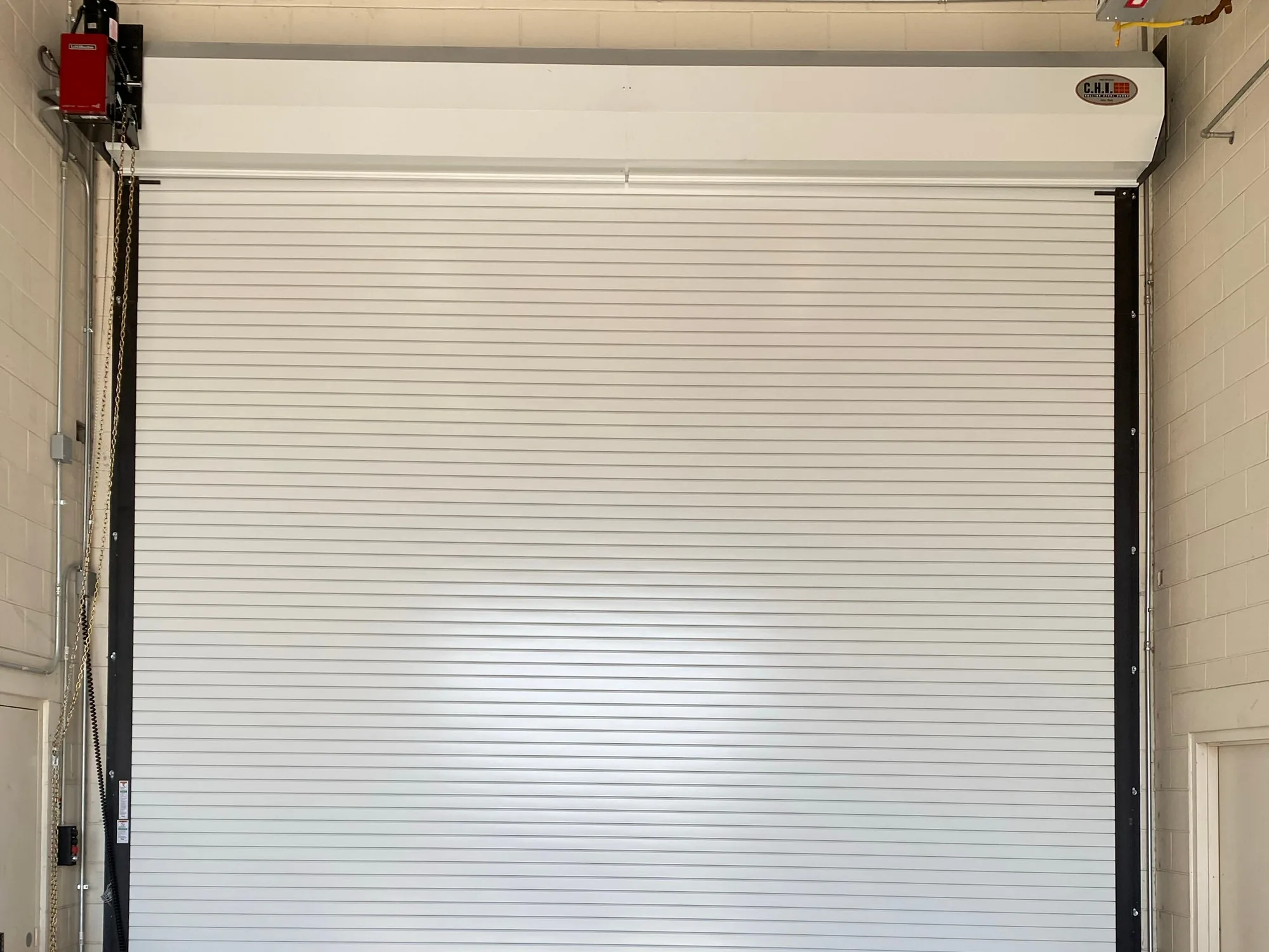 White rolling steel door closed inside a concrete block commercial bay, with the chain hoist at the side