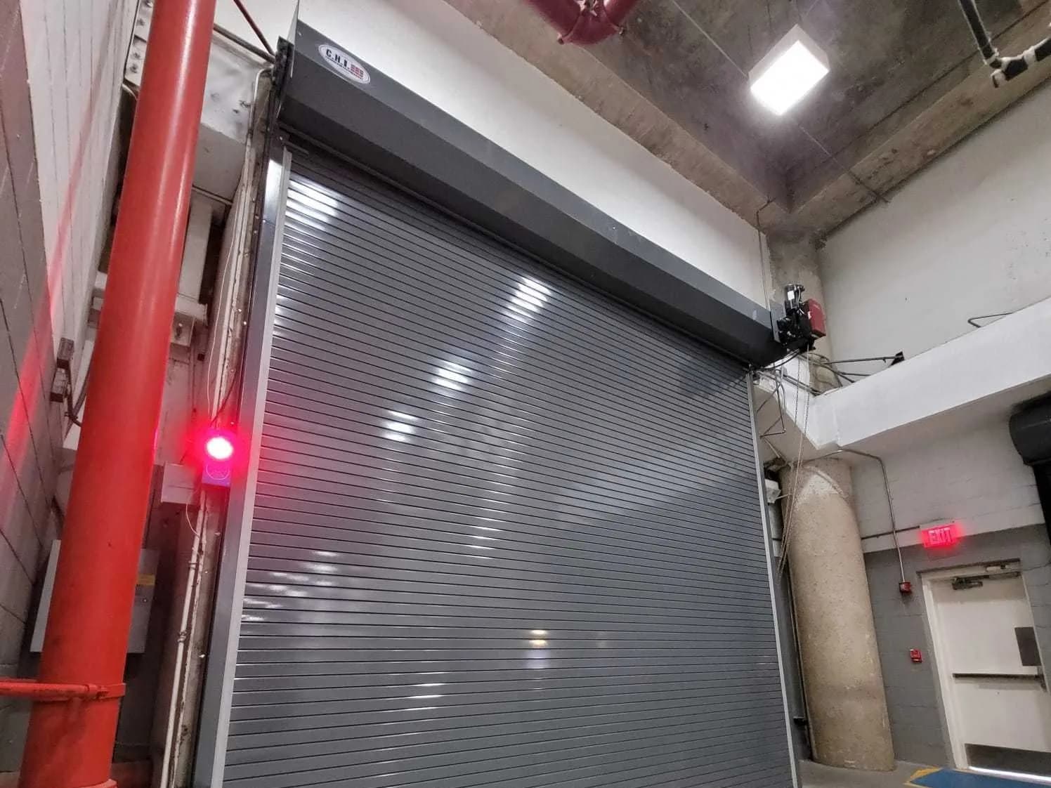 Grey rolling steel door closed across an interior drive lane, with a red standpipe alongside