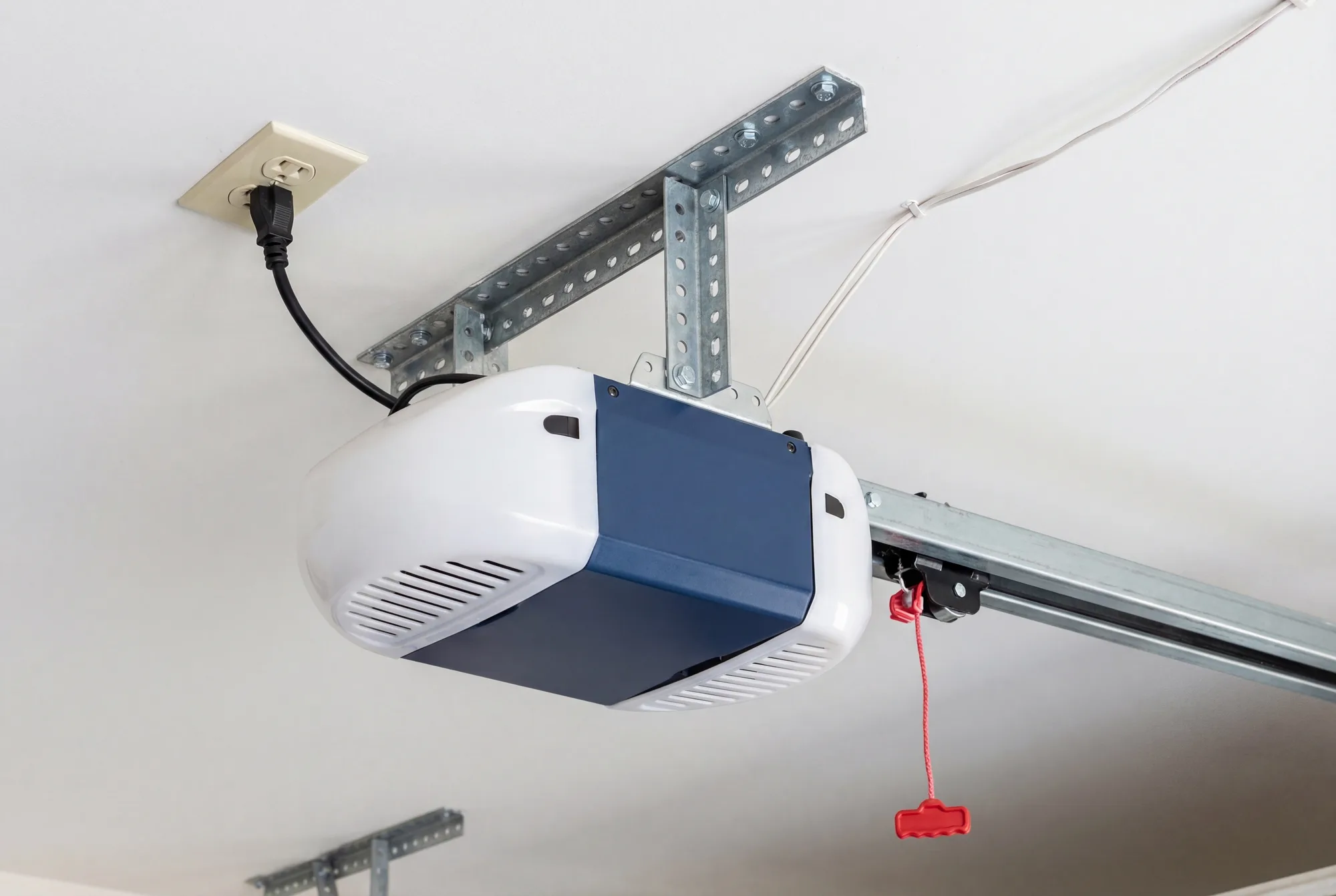 Belt-drive garage door opener head mounted to a garage ceiling with its rail, trolley, and red emergency release handle