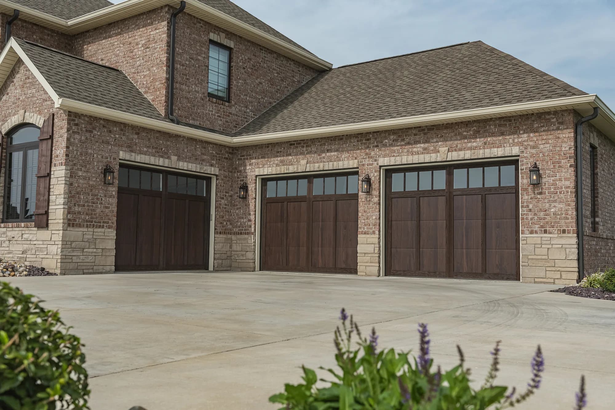Three woodtone overlay garage doors with windows on a brick home, seen straight on