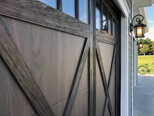 Weathered wood-look garage door with X-brace overlay boards and a coach-style lantern