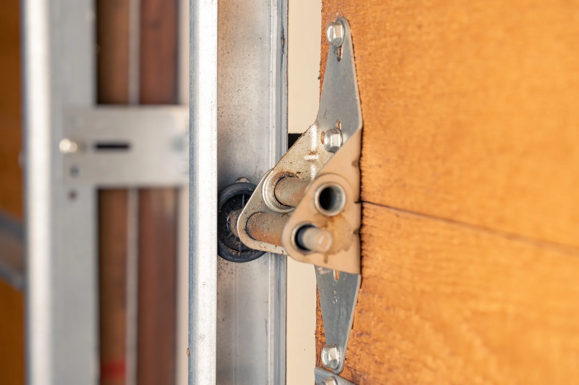 Close-up of a garage door roller and hinge bracket bolted to a wood-look panel, with the roller seated in the vertical track