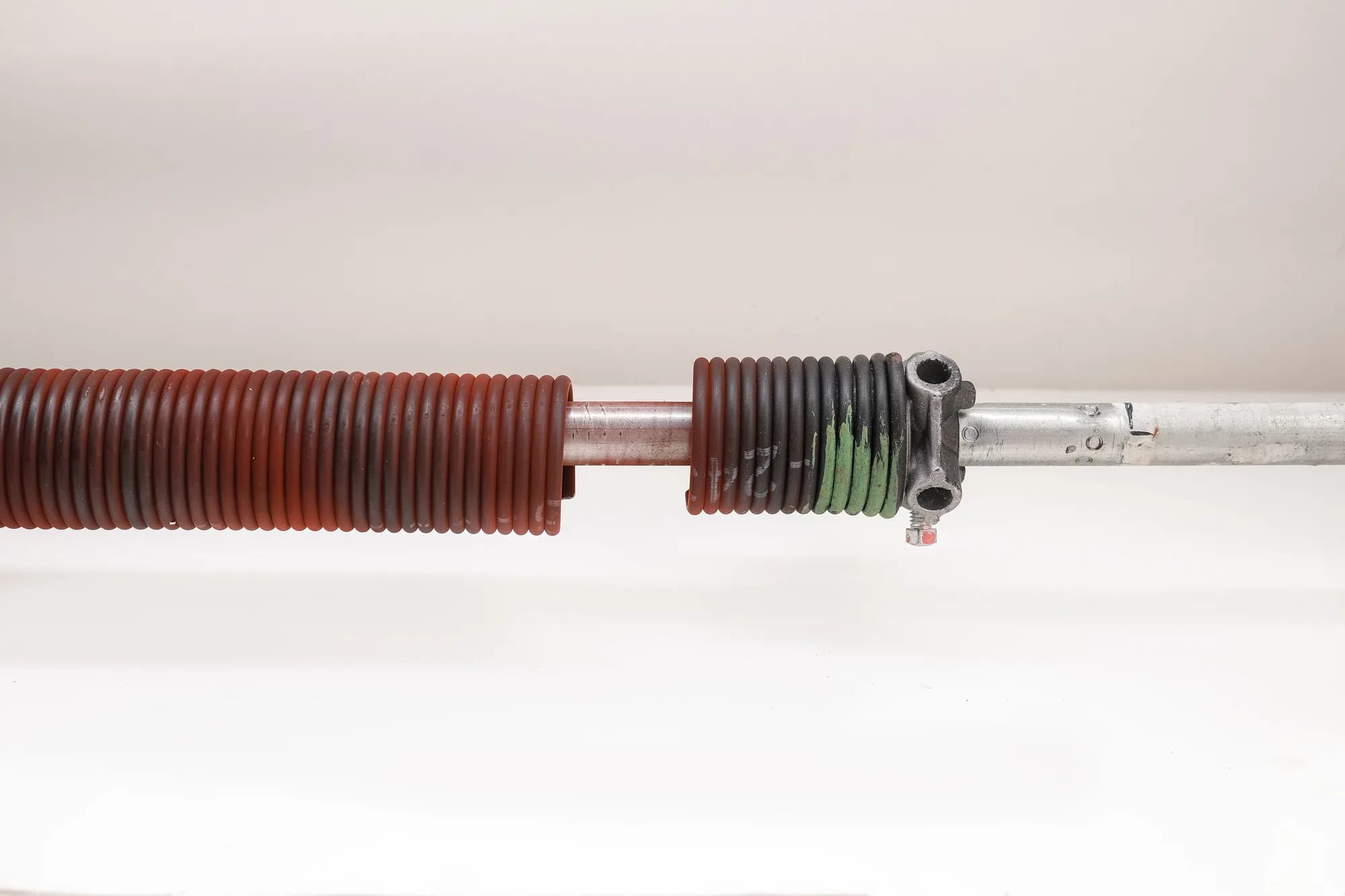 Two garage door torsion springs, one red-coded and one green-coded, mounted on a steel shaft with the centre bearing plate between them