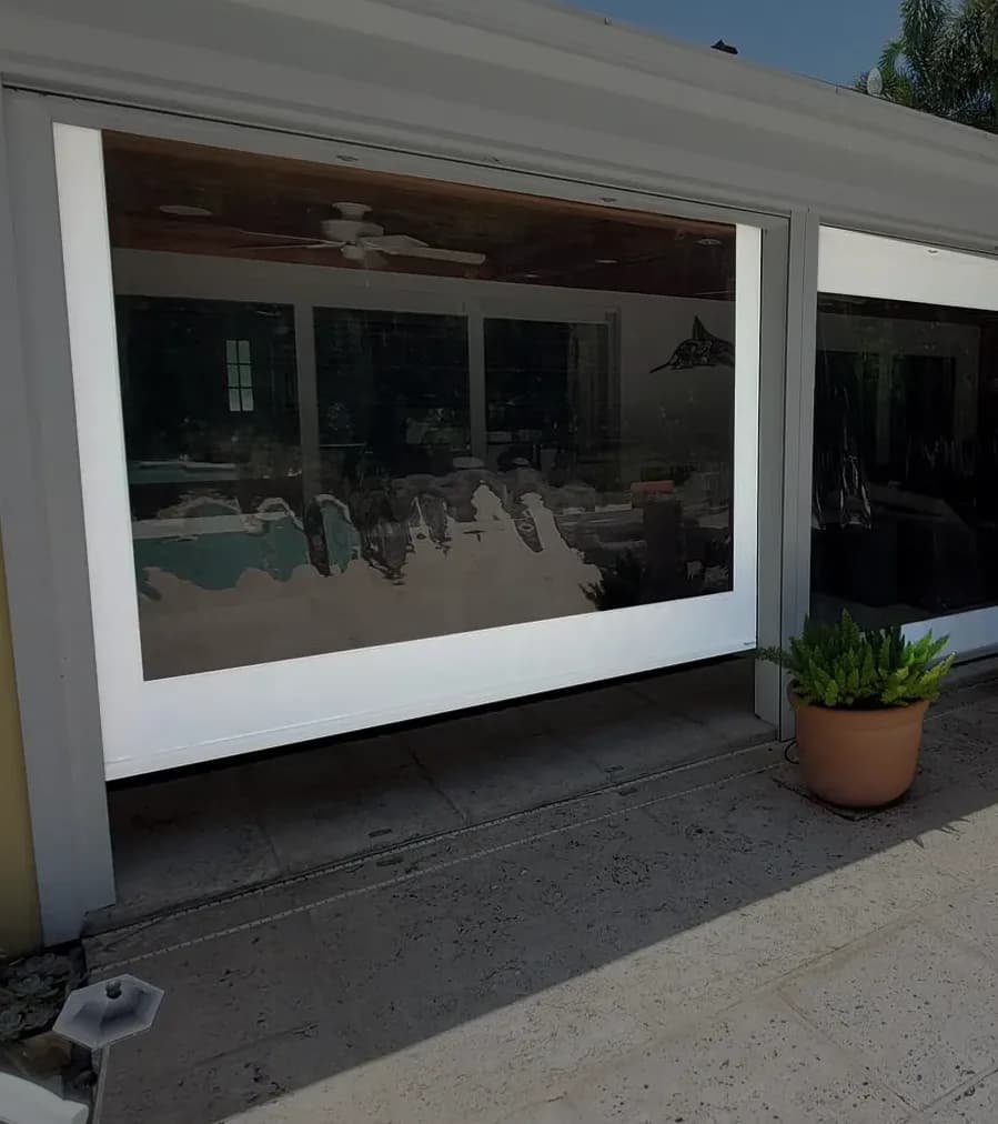 Close view of a lowered clear vinyl screen panel with a wide white Weblon border, seated in its side track, reflecting the covered patio behind it
