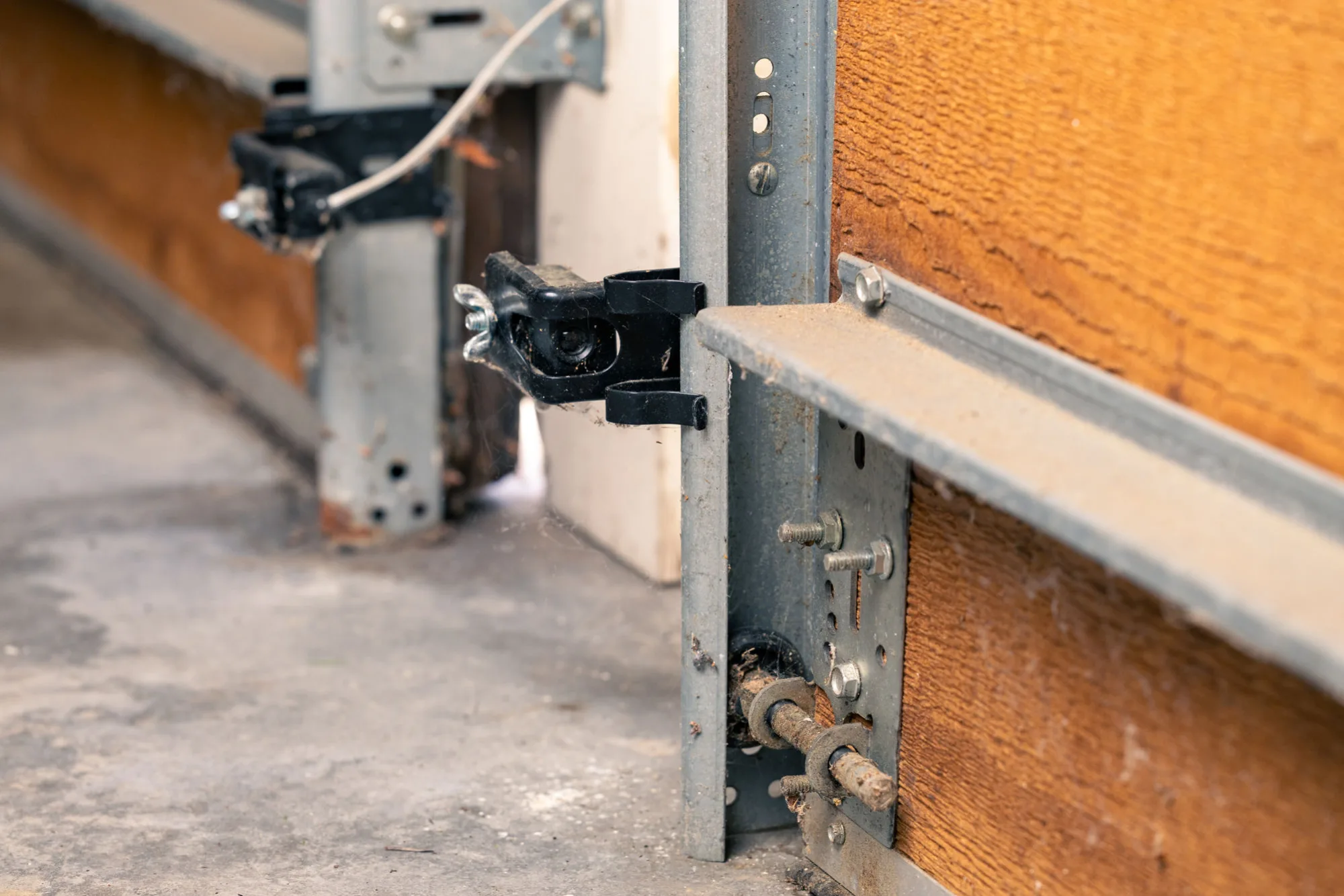 Close-up of a garage door roller, hinge bracket, and vertical track bolted to the door jamb